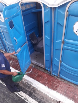 Homem limpando o interior da porta de um banheiro químico