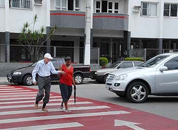 Mulher conduz idoso sobre a faixa de pedestres